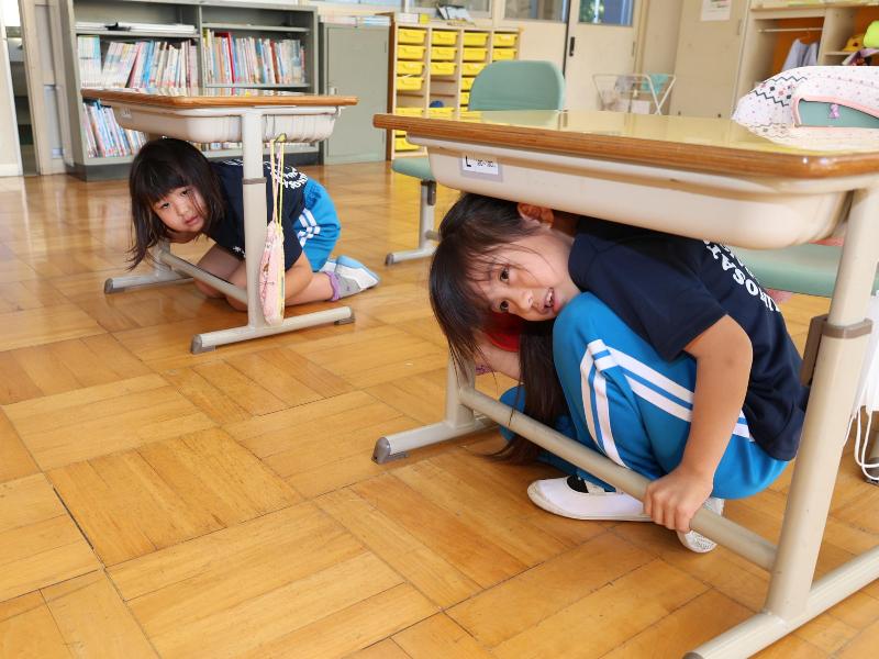 机の下に避難する児童