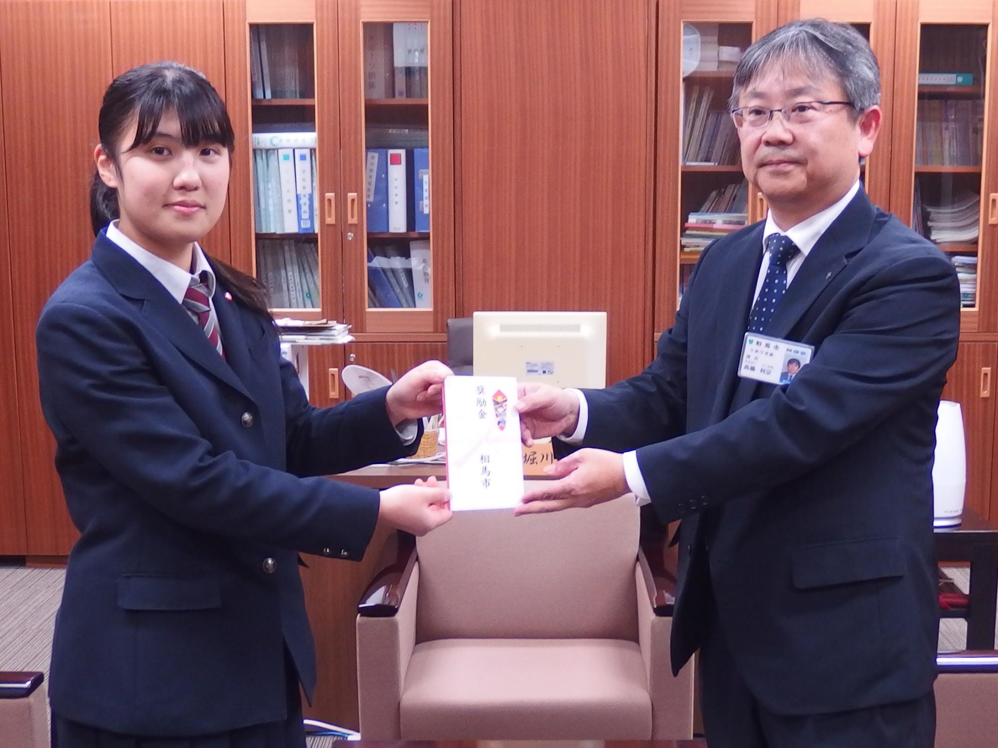 奨励金を受け取る羽根田有華さんと手渡す高橋生涯学習課長の様子