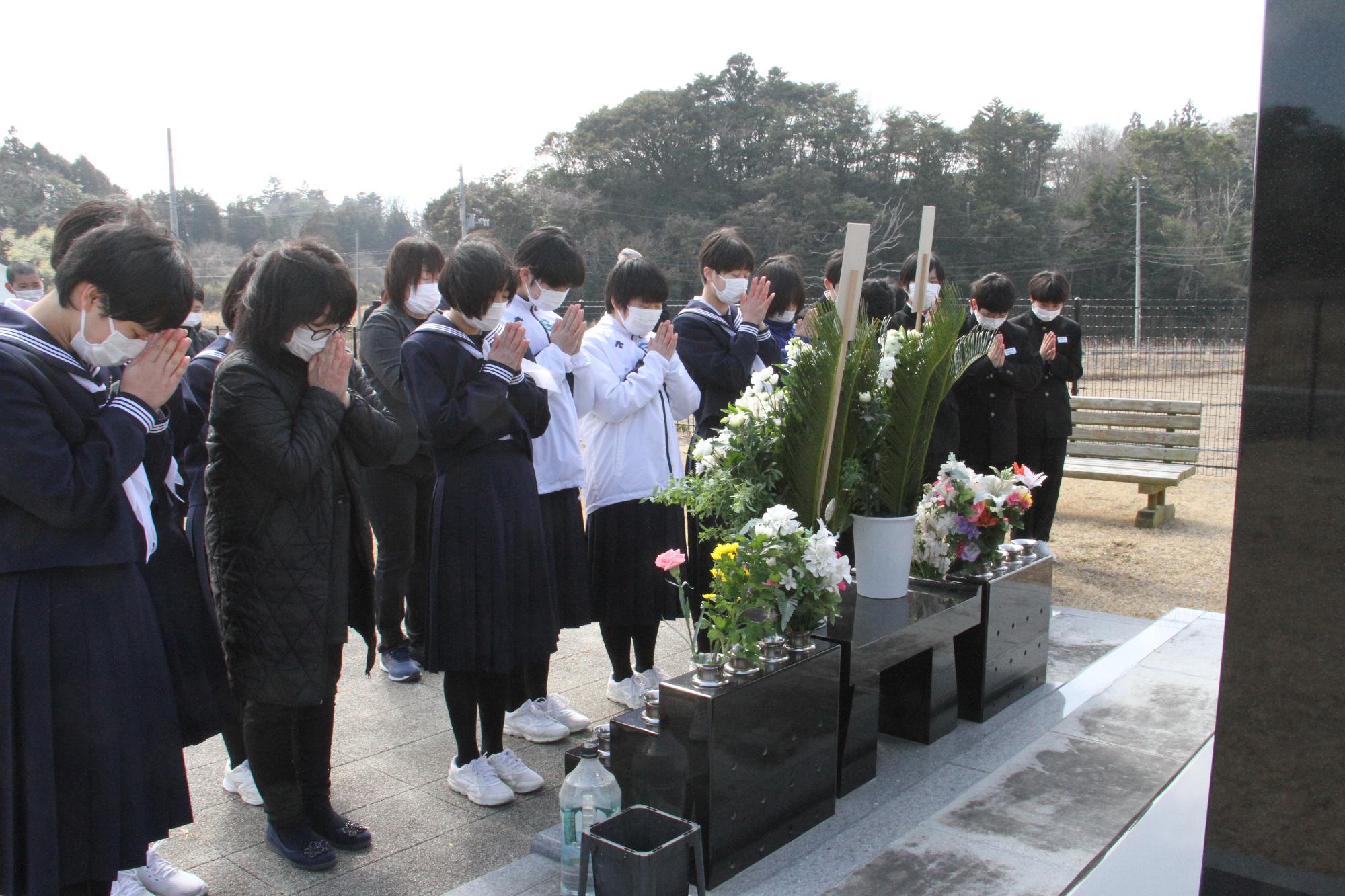 生徒らが震災の慰霊碑の前で手を合わせる様子