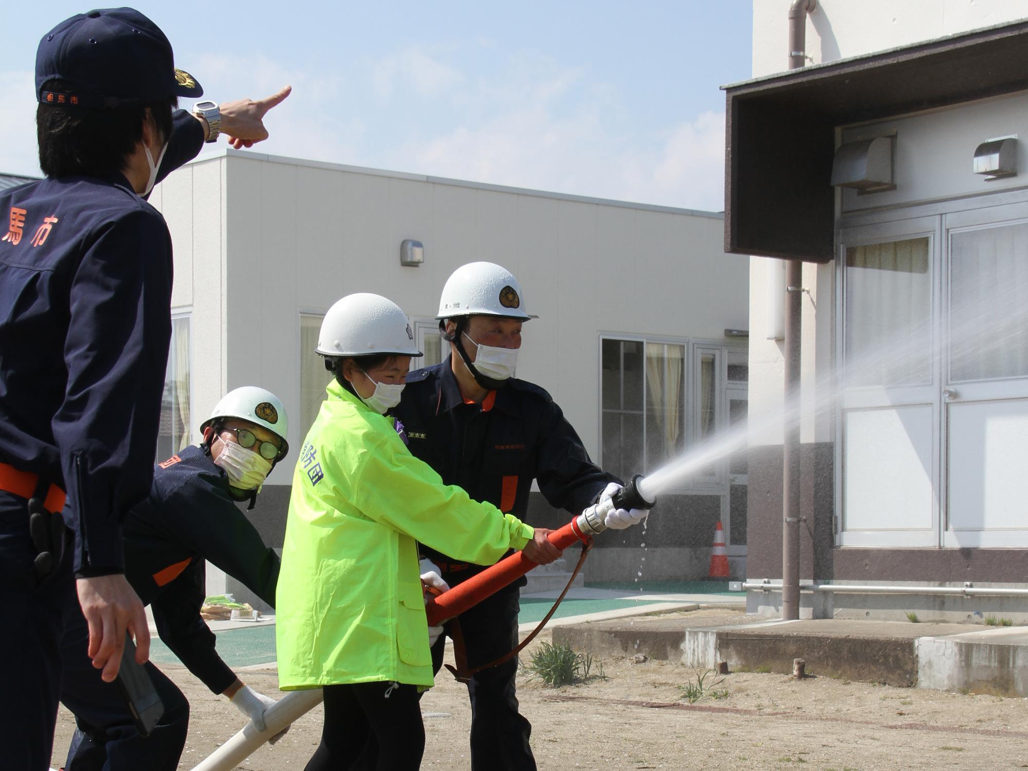 日立木小学校避難訓練で代表児童が消防団員の補助の下、放水体験を行う様子